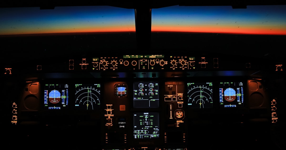 An airliner flight deck at night, instrument panels glowing against the horizon