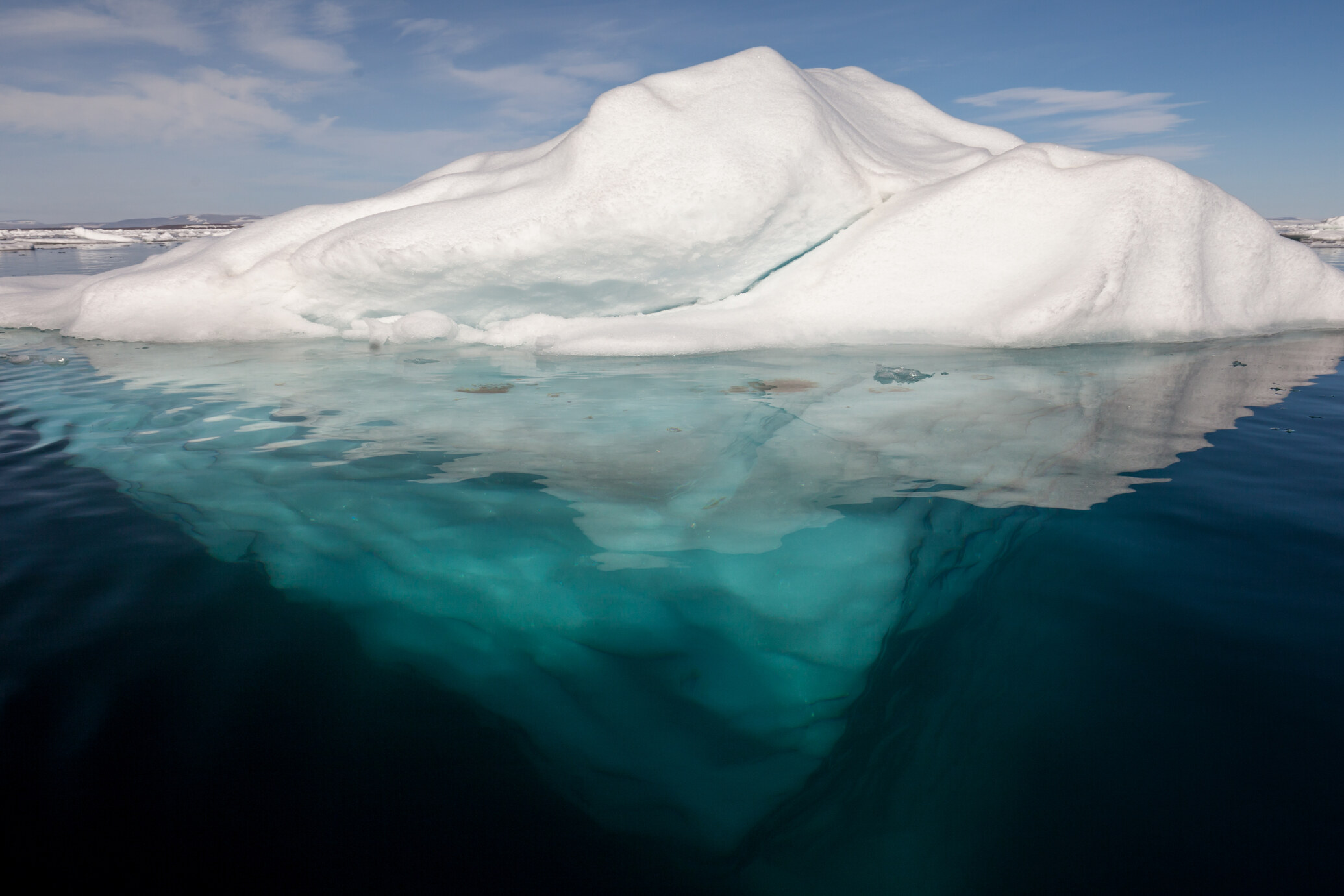 An Arctic iceberg in clear water with its large underside visible beneath the surface