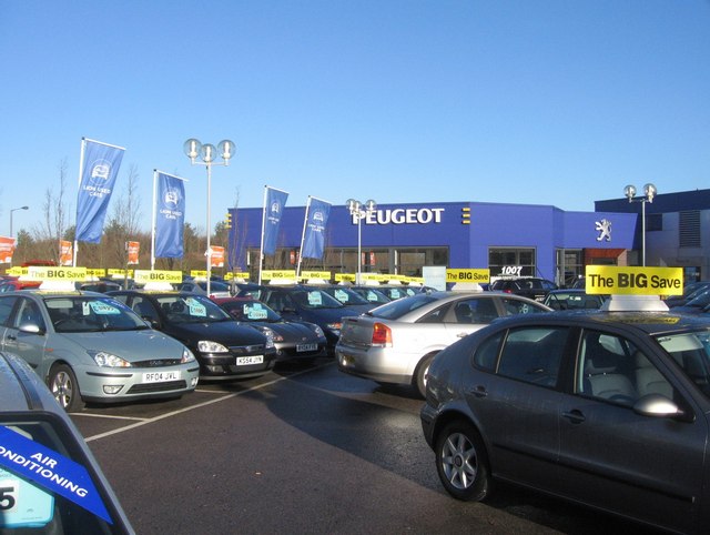 A sunny UK car dealership forecourt with rows of cars for sale